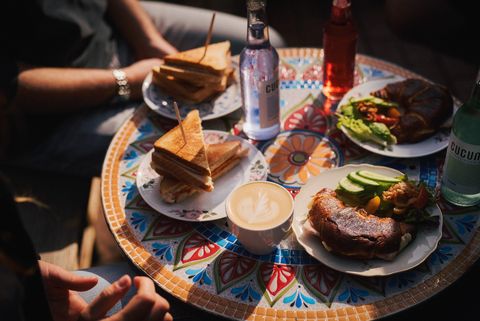 Bunter Mosaiktisch mit Sandwiches, Croissants, Kaffee und Getränken zum Frühstück. 