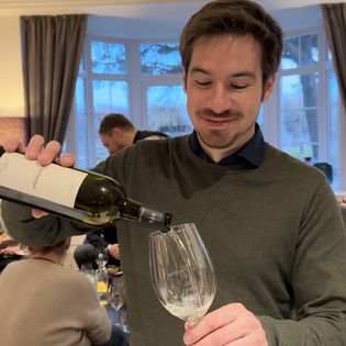 Mann gießt Weißwein in Glas