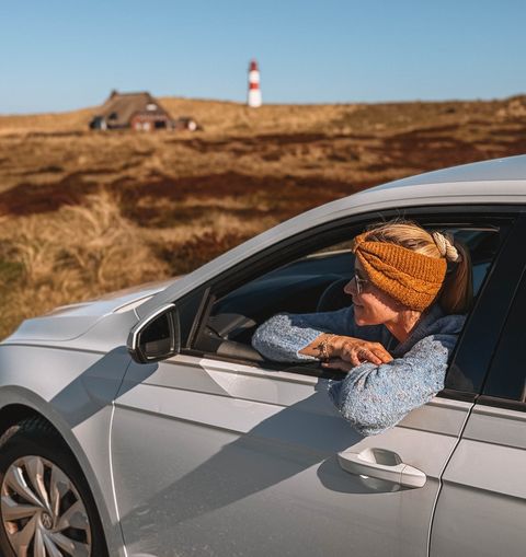 Frau blickt aus Mietwagenfenster vor Dünen und Leuchtturm auf Sylt.