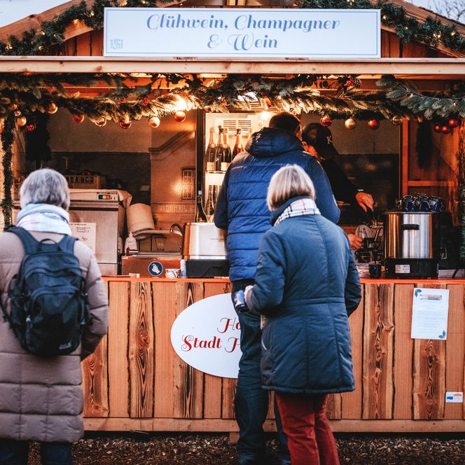 Besucher kaufen Glühwein und Champagner an einem festlich dekorierten Holzstand.