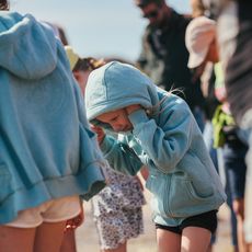 Kinder in Kapuzenjacken auf einer Wattwanderung, ein Mädchen hält sich die Ohren zu. 