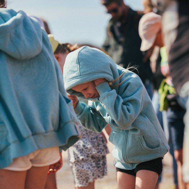 Kinder in Kapuzenjacken auf einer Wattwanderung, ein Mädchen hält sich die Ohren zu. 