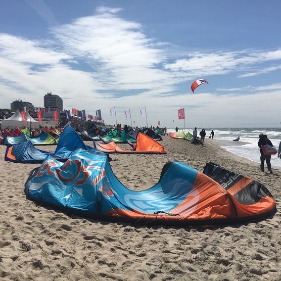 Bunte Kites am Strand mit Menschen, Meer und Eventzelten im Hintergrund