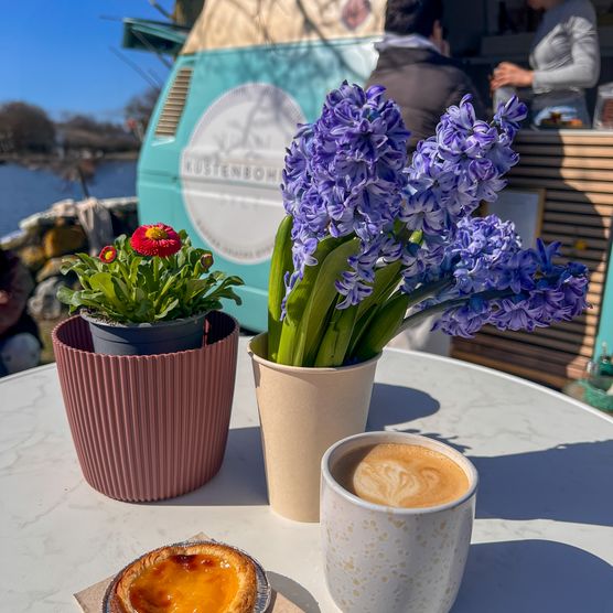 Kaffee, Pastel de Nata und frische Blumen auf einem Tisch