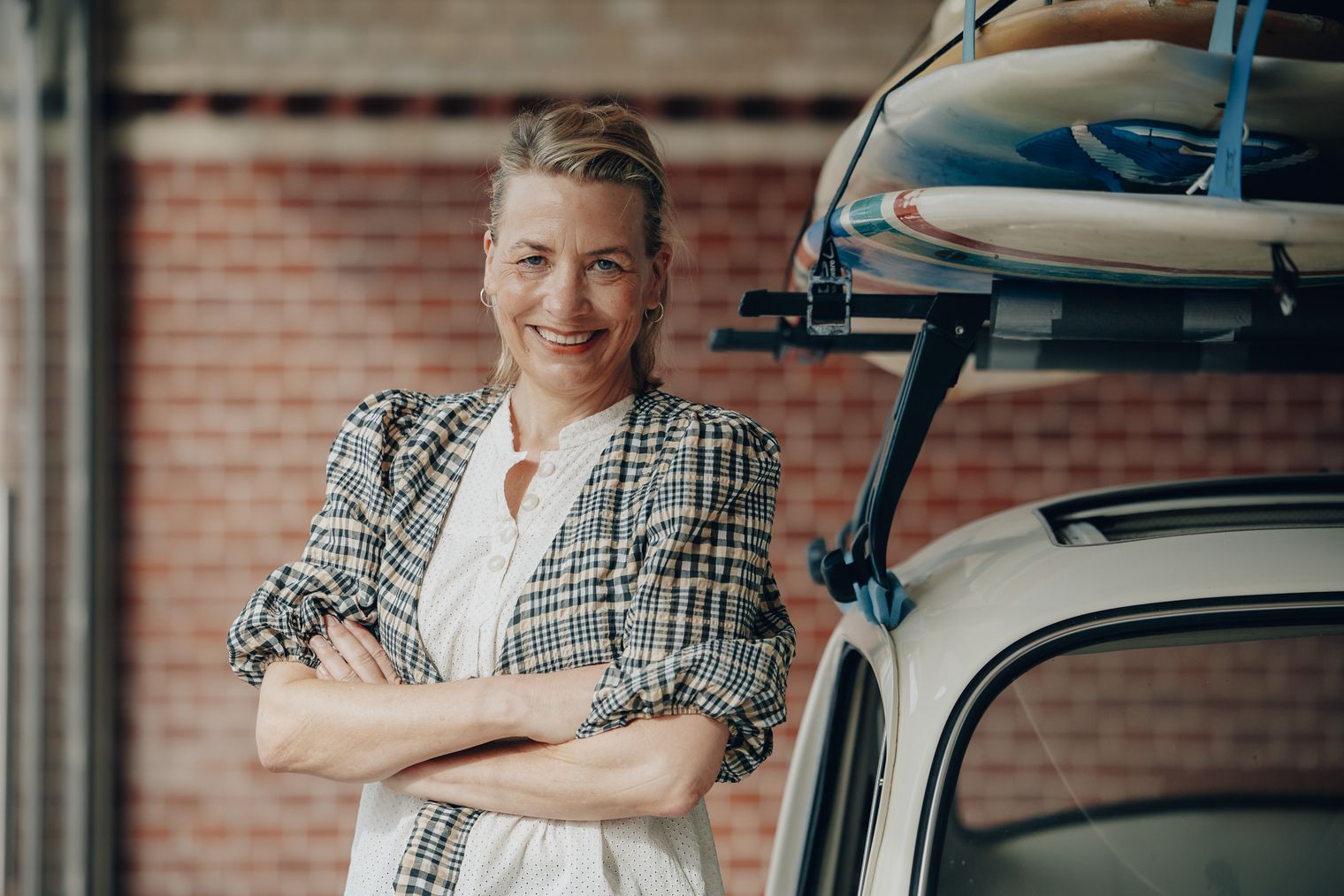 Jutta Vielberg steht lächelnd mit verschränkten Armen neben einem Fahrzeug mit Dachträger und Boards.