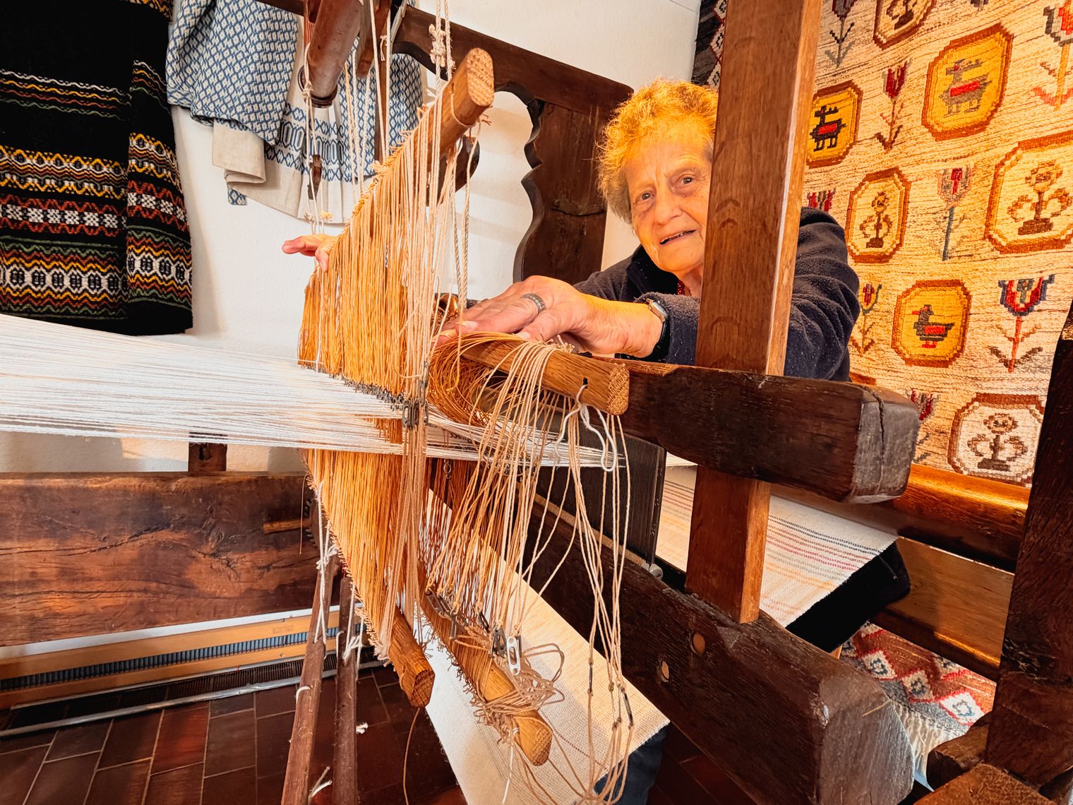Ältere Frau richtet Fäden an einem großen Holzwebstuhl ein.