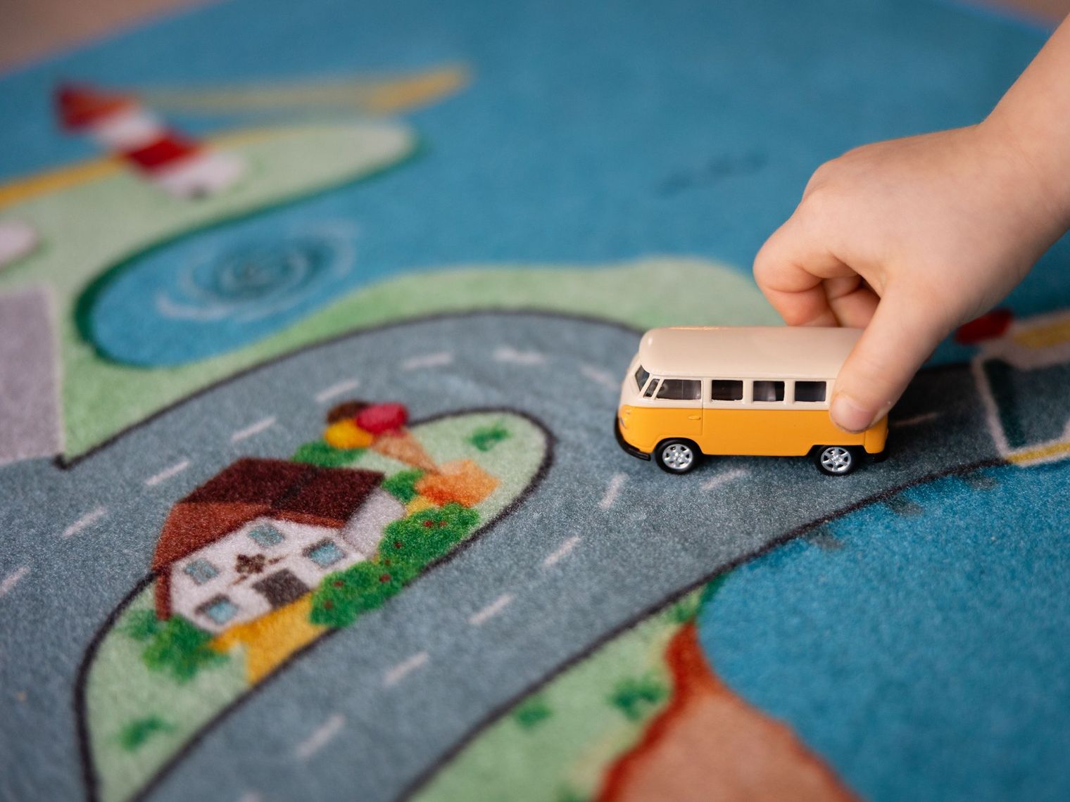Kinderhand bewegt gelbes Spielzeugauto auf Sylter Straßenmotiv-Spielteppich.