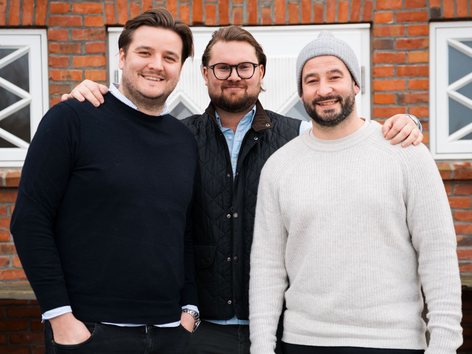 Drei Männer lächelnd vor Backsteinfassade