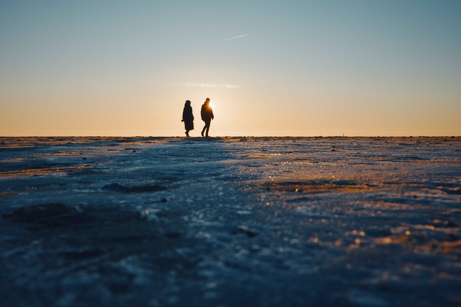 Zwei Menschen spazieren bei Sonnenuntergang über einen vereisten Strand