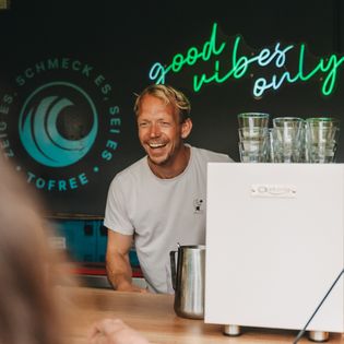 Mann lacht hinter Getränkestand mit Neon-Schrift