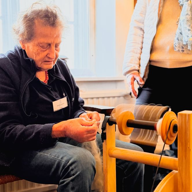 Ältere Frau hält Wollfasern und spinnt sorgfältig.