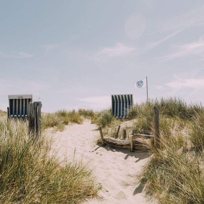 Zwei Strandkörbe in Dünenlandschaft mit Sandweg und wehender Fahne