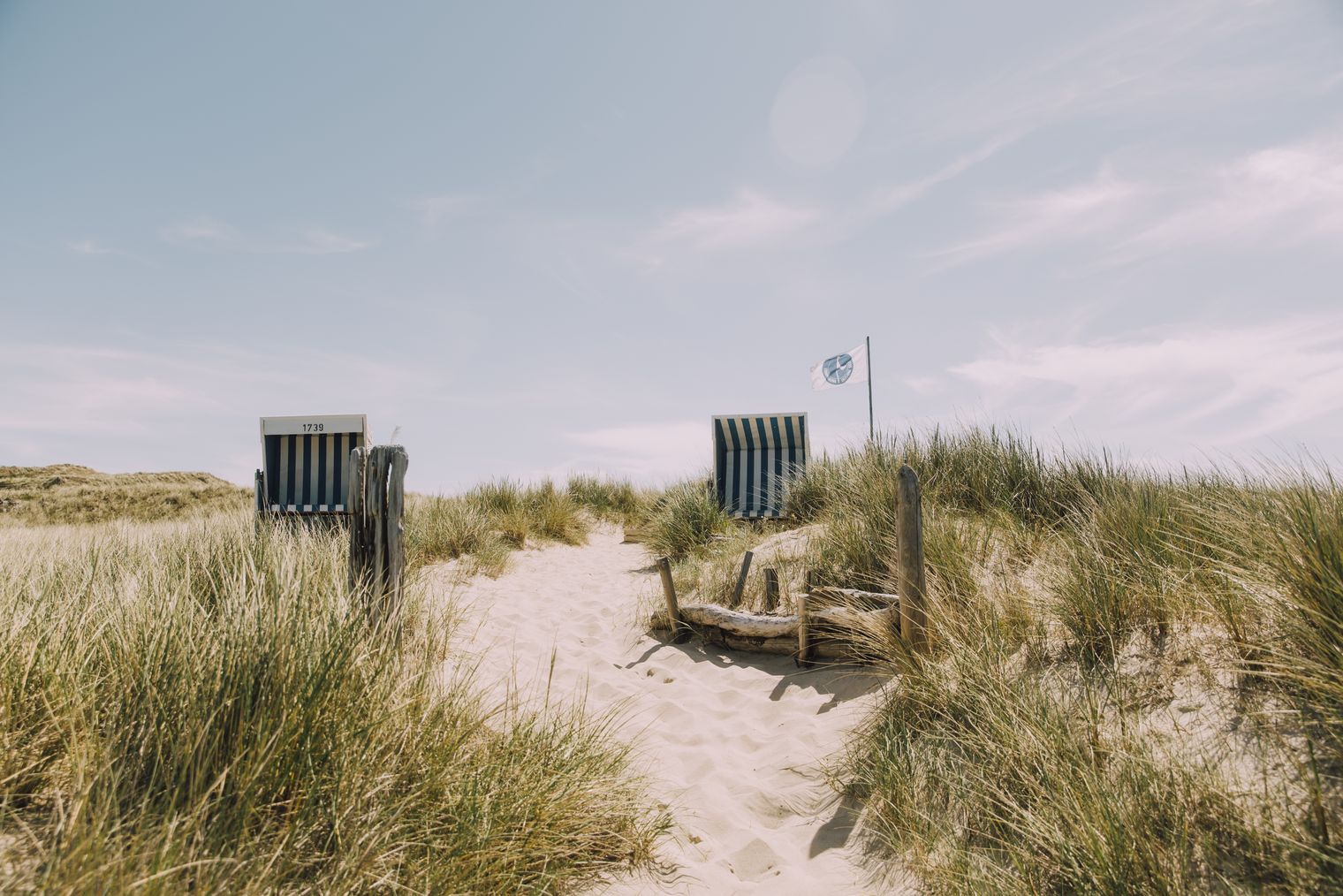 Zwei Strandkörbe in Dünenlandschaft mit Sandweg und wehender Fahne