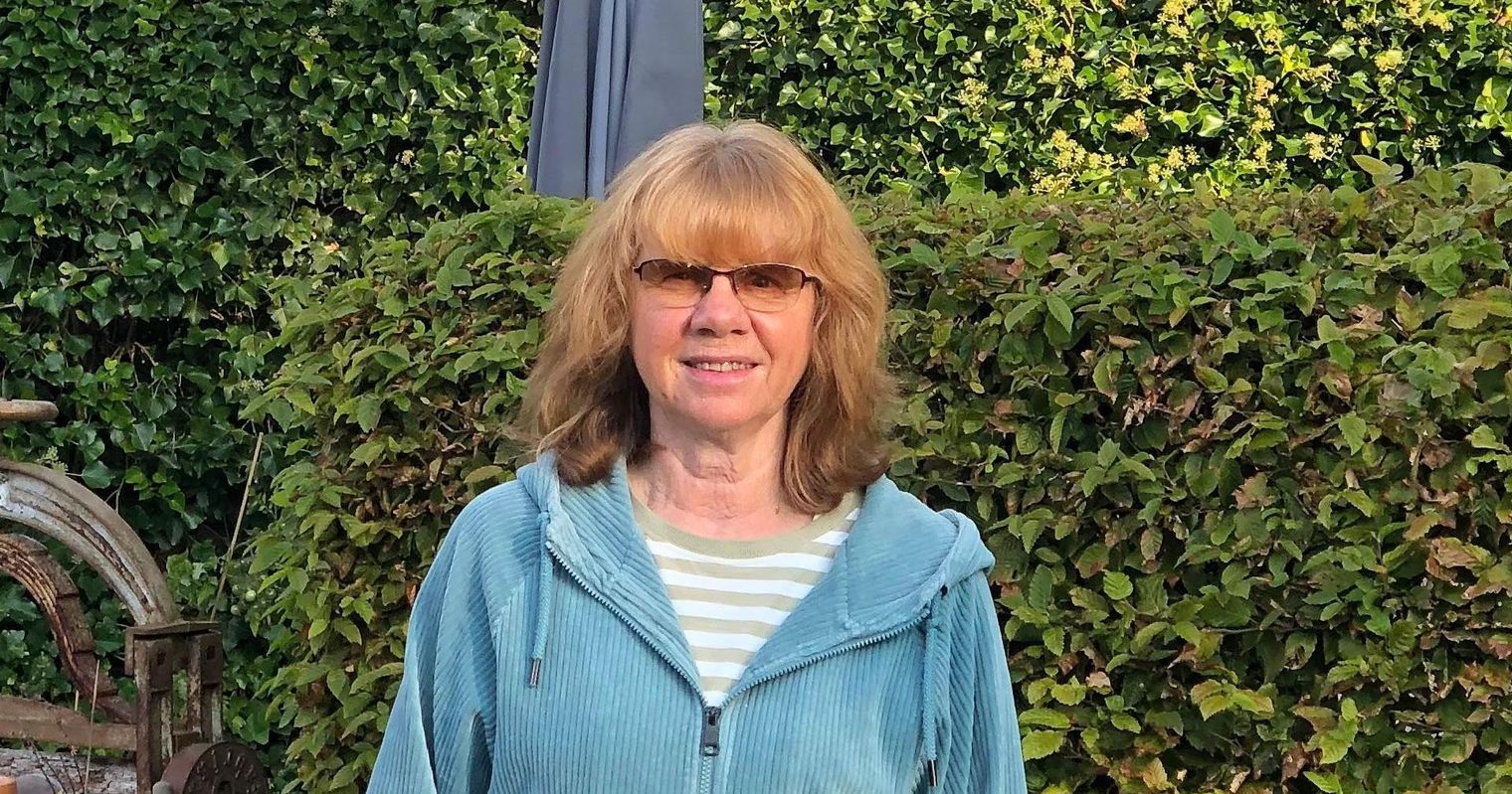 Dörte Lindner-Schmidt steht im Garten vor einer Hecke und einem Kirchturm.