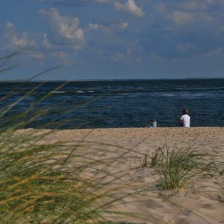Mann sitzt im Sand und blickt aufs Meer