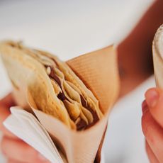Crêpe mit Schokolade und Glas Kaffee in den Händen gehalten.