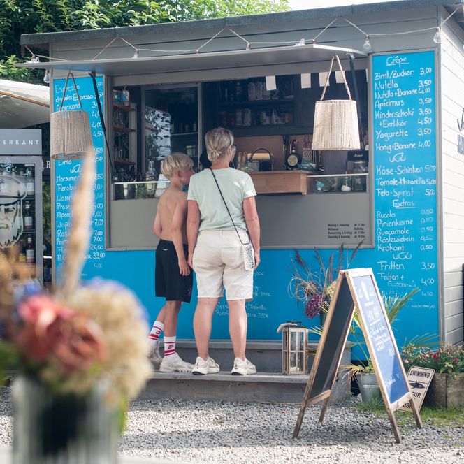 Frau und Kind bestellen an einem blauen Foodtruck mit Menütafeln.