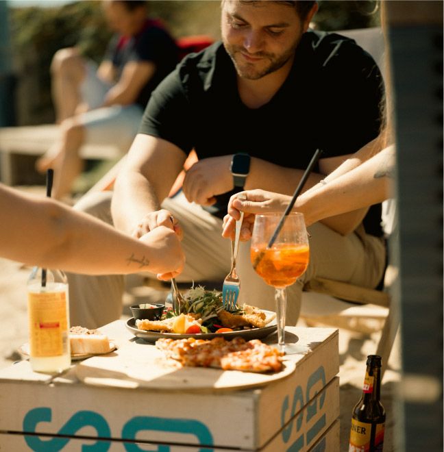 Menschen essen gemeinsam draußen an improvisiertem Tisch.