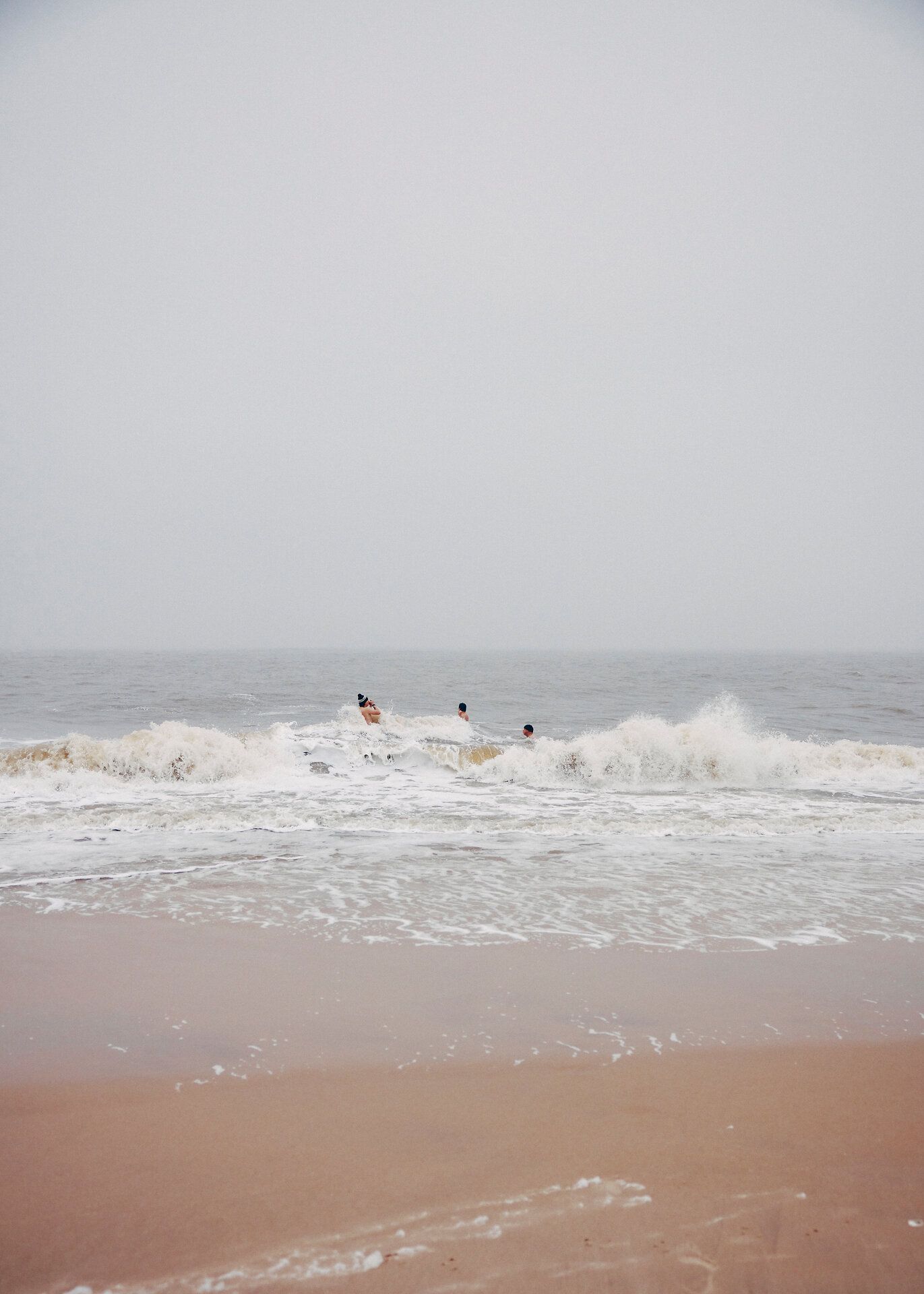Drei Männer schwimmen im Winter in der Nordsee bei starker Brandung.
