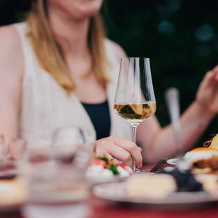 Hand hält Weinglas, Essen auf einem gedeckten Tisch.