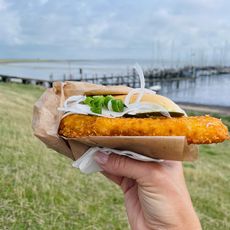 Hand hält ein Fischbrötchen vor dem Hafen von Rantum.