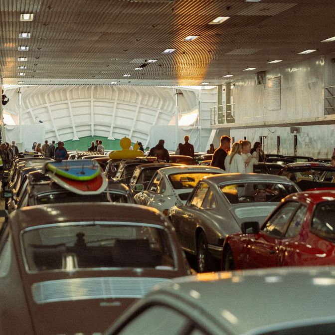 Dicht geparkte Porsches auf einer Fähre mit Menschen und Surfbrettern.