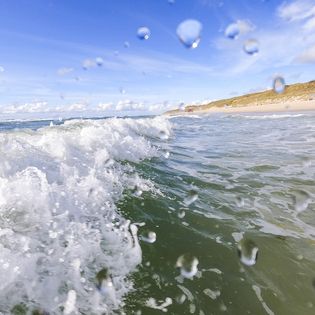 Wellen mit Wassertropfen und Sandstrand bei Wenningstedt auf Sylt.