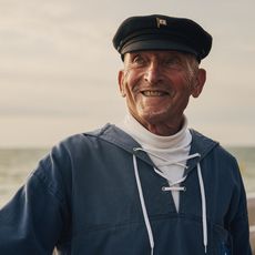 Ein echter Sylter: Lächeln mit Nordseebrise Portrait eines lächelnden älteren Mannes in traditioneller Seemannskleidung mit Kapitänsmütze.