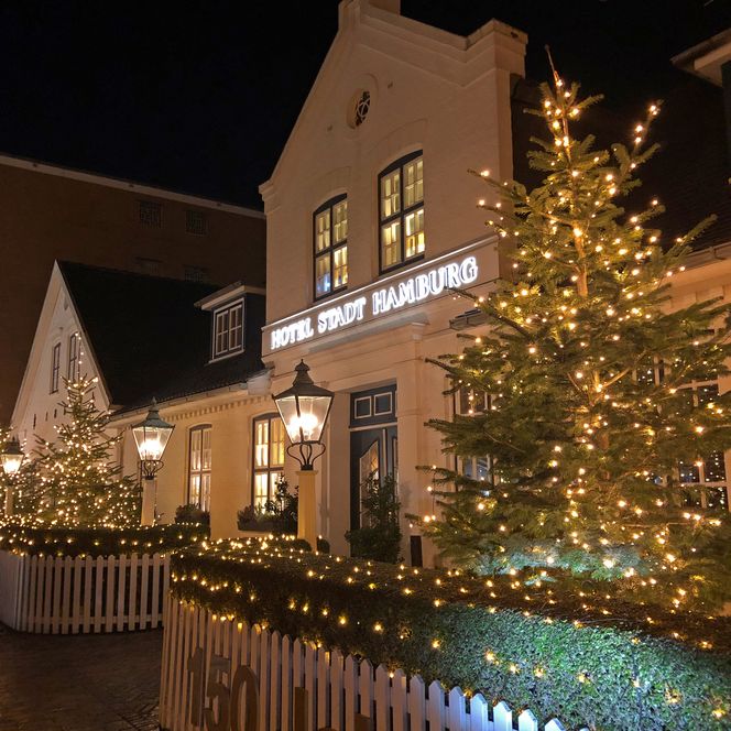 Festlich beleuchtetes Hotel Stadt Hamburg in Westerland mit Weihnachtsbäumen und Lichterketten.