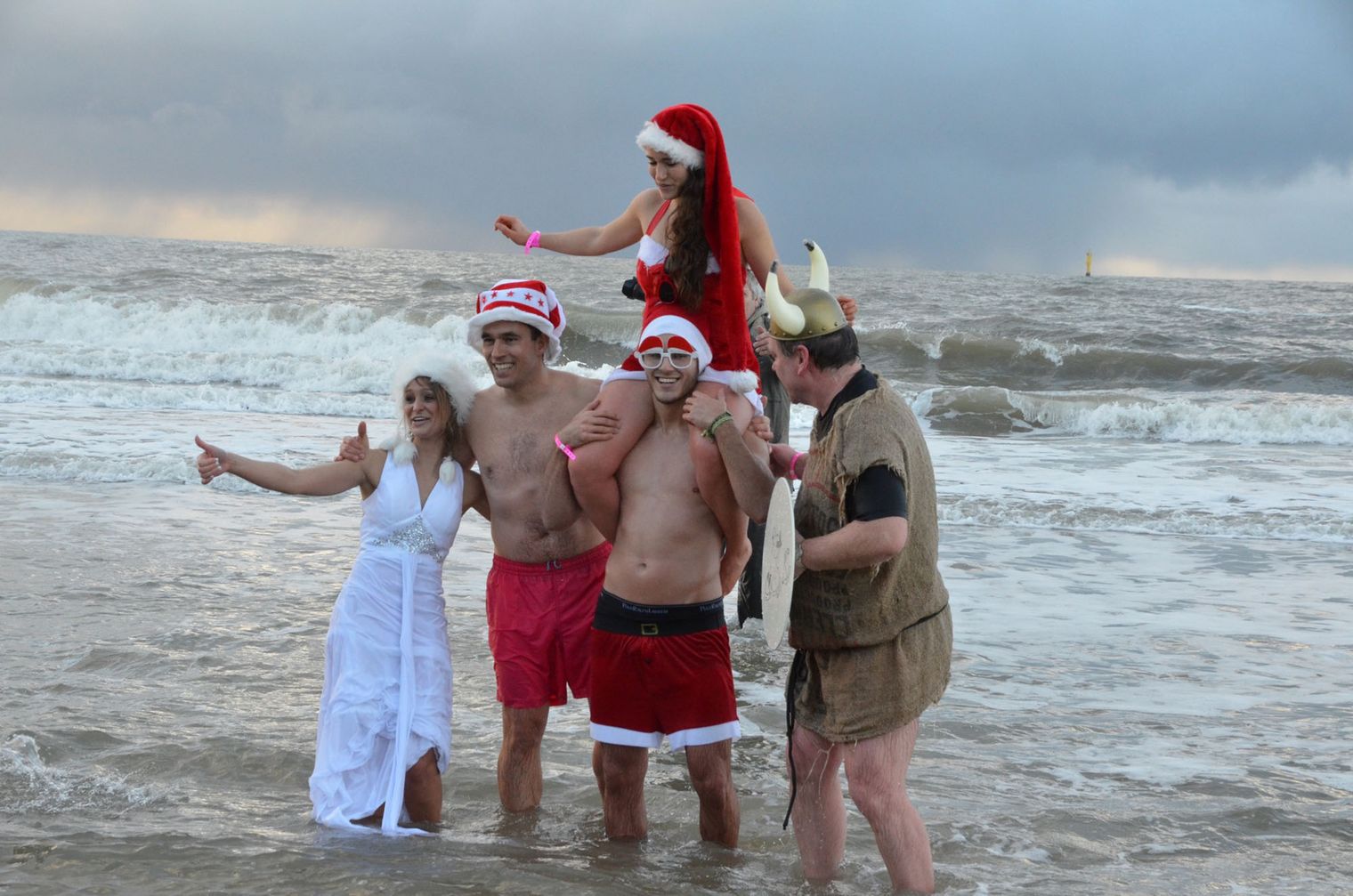 Menschen in Weihnachtskostümen und lustigen Verkleidungen nehmen am winterlichen Weihnachtbaden im Meer teil.