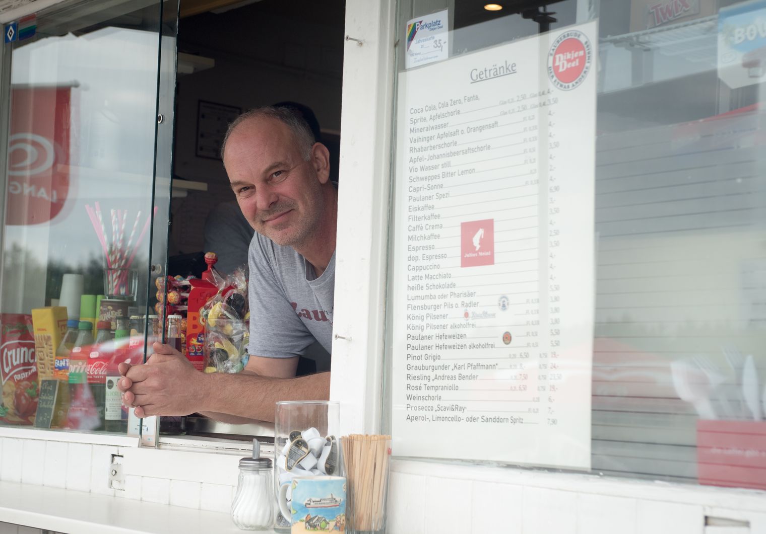 Mann schaut freundlich lächelnd aus dem Verkaufsfenster seines Kiosks.