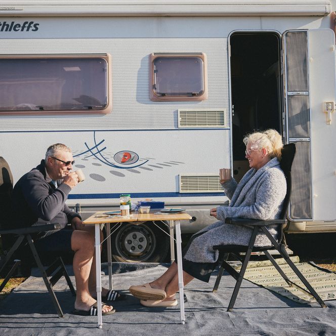 Paar sitzt vor ihrem Wohnmobil und genießt Kaffee.