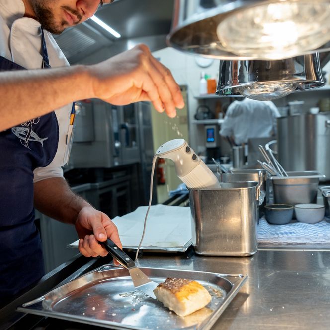 Koch würzt ein Fischfilet konzentriert in der Restaurantküche.