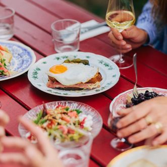 Verschiedene Speisen, darunter Käse, Kartoffeln und Brot, auf einem rot lackierten Tisch im Käseklub in Keitum auf Sylt, mit Gläsern Wein und Wasser.