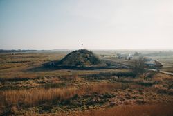 Biikehaufen in weiter Landschaft, Menschen und Fahrzeuge drumherum