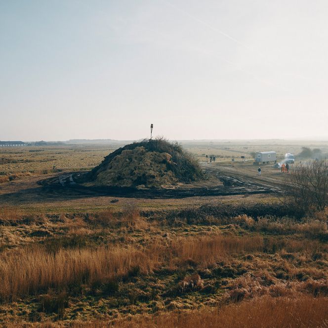 Biikehaufen in weiter Landschaft, Menschen und Fahrzeuge drumherum