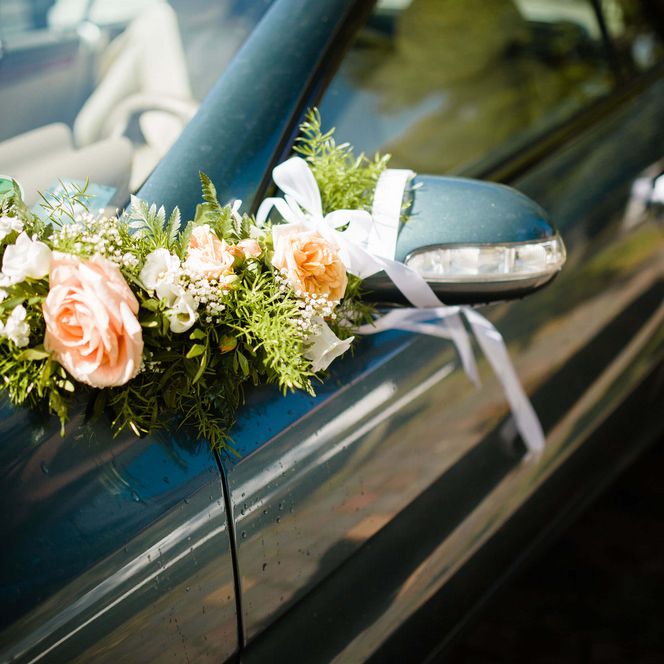 Rosafarbene Hochzeitsblumen mit Schleifen am Seitenspiegel eines Autos