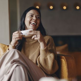 Lachende Frau mit Teetasse in gemütlicher Sitzecke