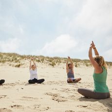 Yoga-Session am Strand mit drei Teilnehmenden und einer Yogalehrerin