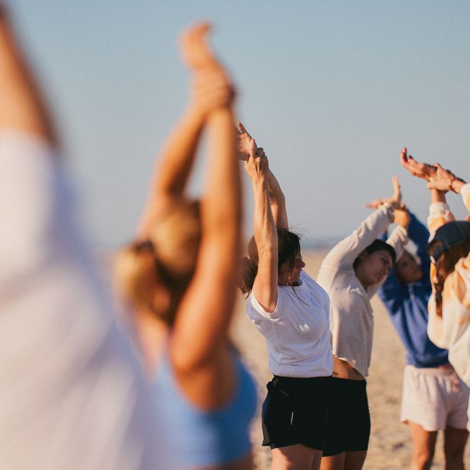 Menschen am Strand in einer dynamischen Yoga-Pose, umgeben von Dünen und der weiten Nordsee.
