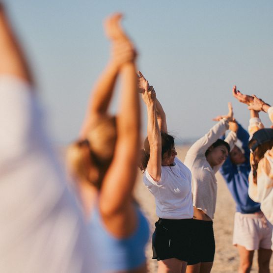 Menschen am Strand in einer dynamischen Yoga-Pose, umgeben von Dünen und der weiten Nordsee.
