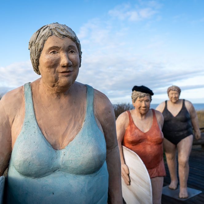 Drei weibliche Skulpturen tragen Surfbretter unter ihren Armen