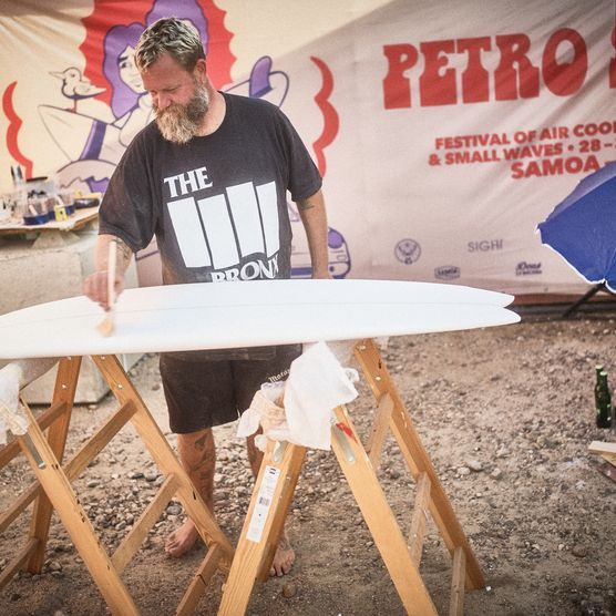 Mann lackiert weißes Surfbrett beim Festivalstan