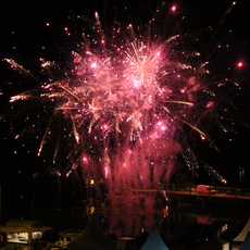 Pinkes und goldenes Feuerwerk über dem Hafen von Hörnum bei Nacht. Im Vordergrund sind Zelte und Lichter am Hafen sichtbar.