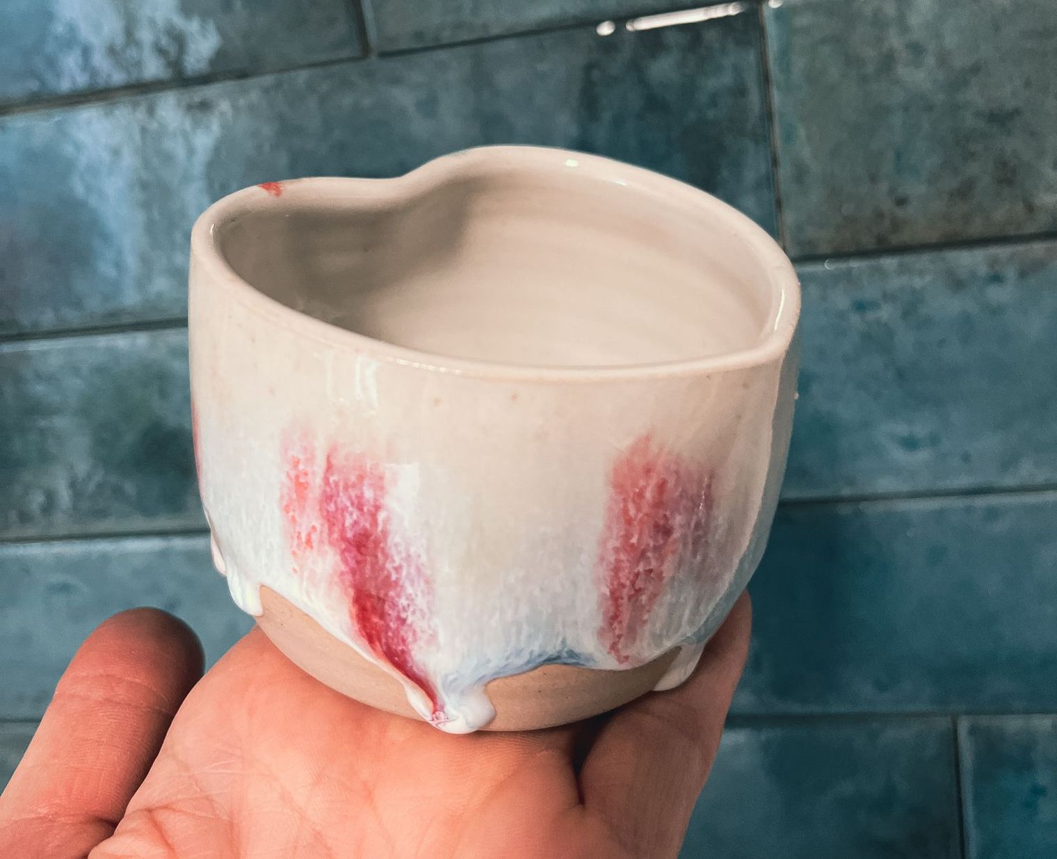 Keramiktasse von Hylli K mit rot-weißer Glasur vor blauer Fliesenwand.