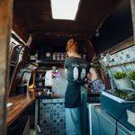 Barista prepares coffee in a stylish coffee bus with wooden elements and tile look.