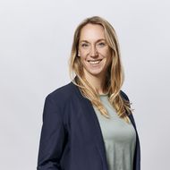 Frau mit blonden Haaren und Blazer lächelt freundlich in die Kamera.