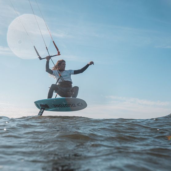 Kitesurferin springt mit Foil-Board über die Wellen vor blauem Himmel.