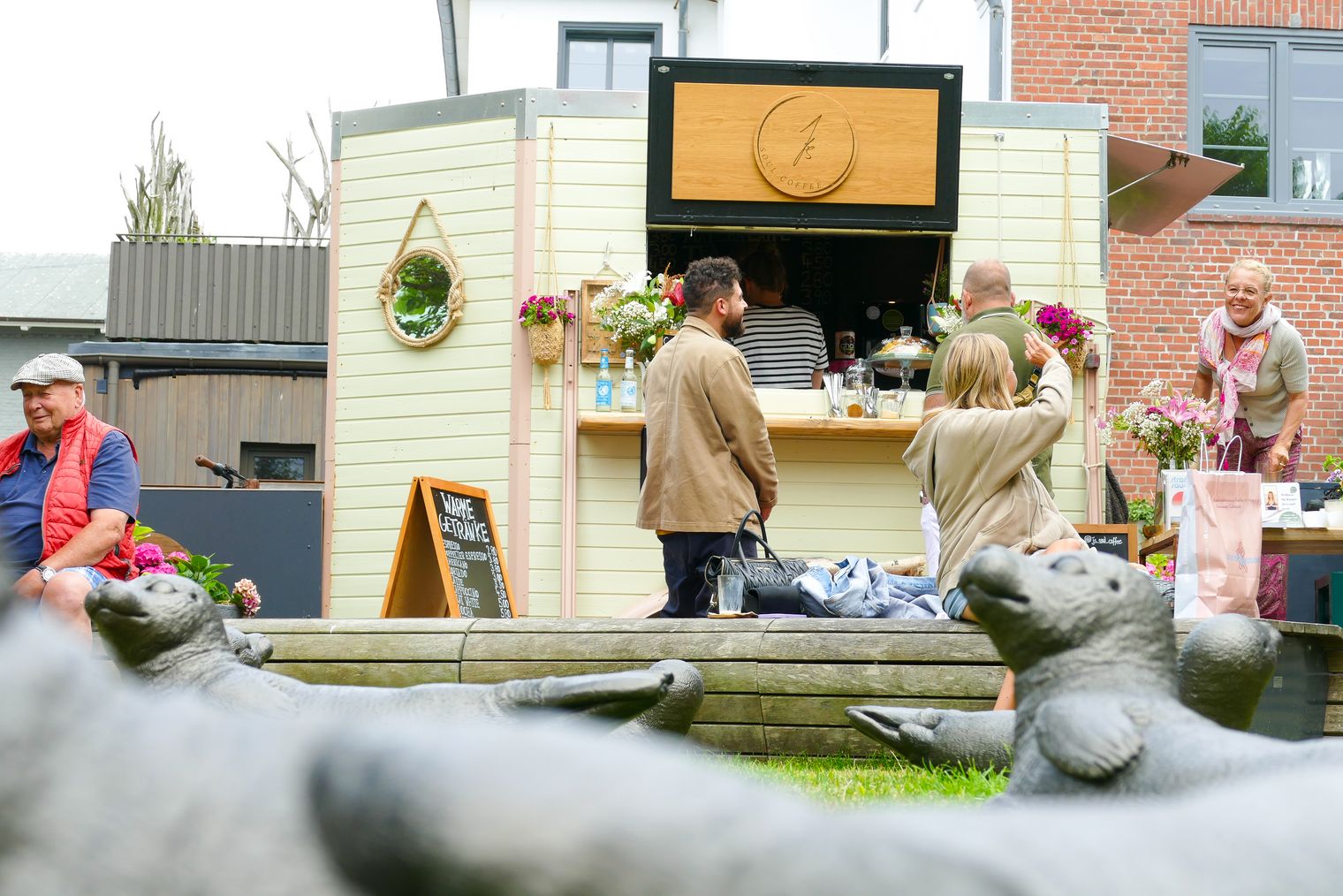Menschen vor Caféstand, im Vordergrund bronzene Robbenskulpturen