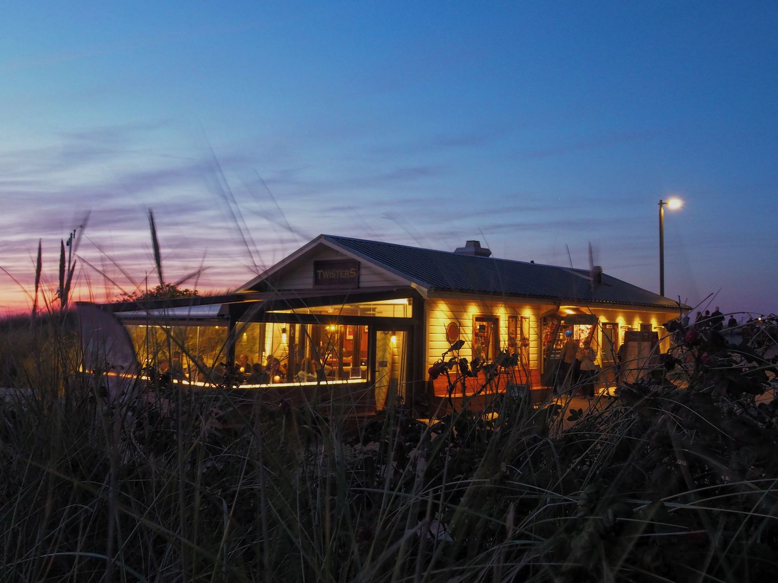 Beleuchtetes Restaurant „Twisters“ in den Dünen bei Sonnenuntergang.